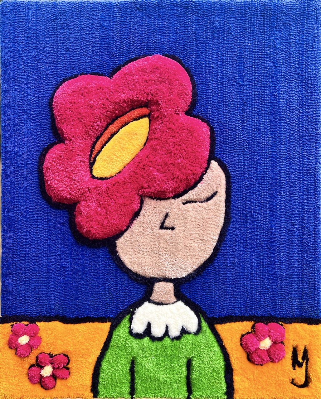 Gros plan texturé sur le tableau en tufting 'Le Fleurissement' de Mari Jinkings, montrant le relief des fibres et les détails du personnage à fleur rose sur fond bleu